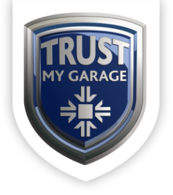 A shield-shaped emblem with a silver border and a blue interior. The words "TRUST MY GARAGE" are inscribed at the top in bold, silver letters. Below the text is a white geometric design resembling a snowflake or an asterisk.